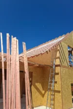 Дом «Игорь» 200 м², Талгар, 2026: по стропилам уложена гидроизоляционная плёнка, смонтированы контробрешётка и обрешётка под металлочерепицу, во фронтоне из СИП-панелей виден проём, к скату приставлена лестница