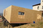 Дом «Аида» 161 м², Бесагаш, 2026: собранная коробка первого этажа из СИП-панелей на стальном ростверке, вид с угла — по низу стен пущен обвязочный брус