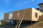 Дом «Аида» 161 м², Бесагаш, 2026: наружная стена из СИП-панелей с проёмами под окна, дом стоит на стальном каркасе-основании, под ним отсыпан щебень