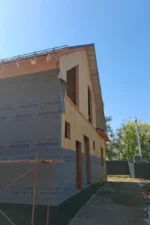 Дом «Игорь» 200 м², Талгар, 2026: торец дома — стены первого этажа обтянуты ветрозащитной мембраной, фронтон мансарды из СИП-панелей с проёмами, свес кровли с подшивкой