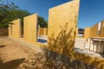 Дом «Сатурин» 165 м², Алматы, 2026: вдоль края плиты выставлены первые панели наружной стены, между ними соединительные стойки, справа сложен запас панелей
